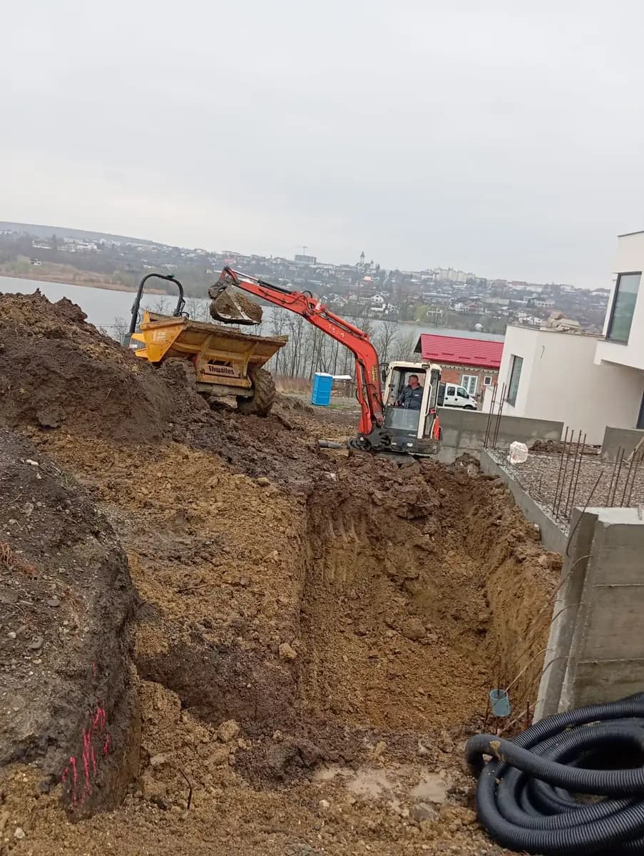 Excavare de fundație pe teren în pantă, cu miniexcavator și basculantă mică pe malul săpăturii