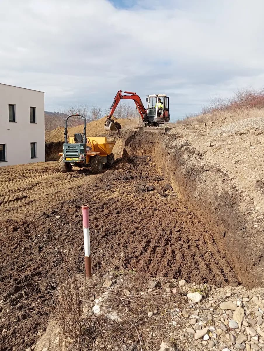 Șanț săpat cu excavatorul pe un teren în pantă, cu pământul așezat pe o singură latură