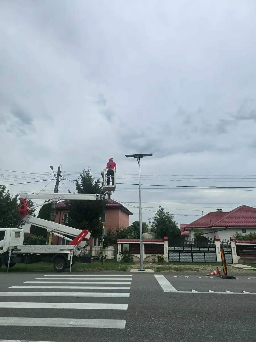 Om în coșul unei nacele, la un corp de iluminat stradal, deasupra unei treceri de pietoni