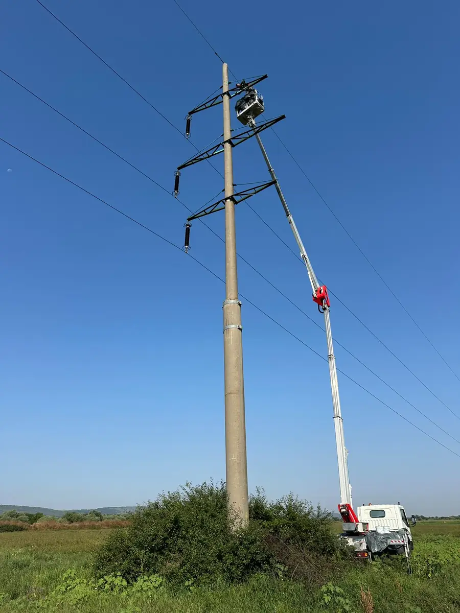 Nacelă cu brațul ridicat până la vârful unui stâlp de electricitate, pe teren neamenajat